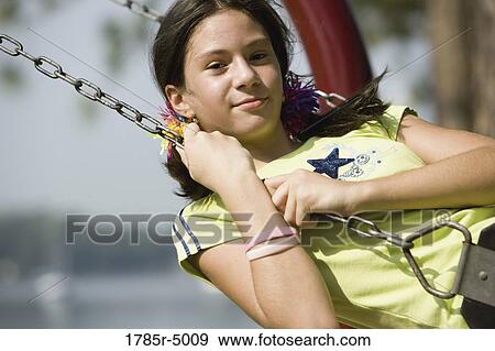 Stock Photo - Portrait of a smiling girl on a swing at a playground. Fotosearch