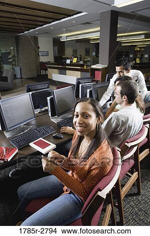 Picture - Portrait of a smiling woman sitting with friends while using computers in the library. Fotosearch
