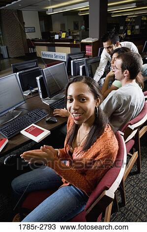 Stock Image - Portrait of a smiling woman sitting with friends while using computers in the library. Fotosearch