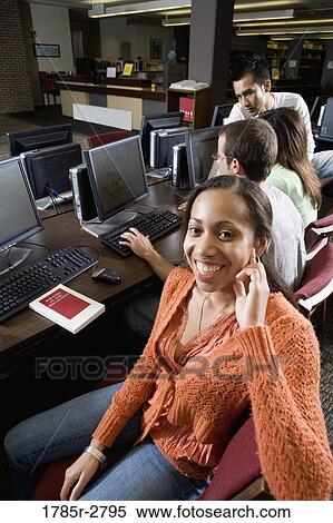 Stock Photography - Portrait of a smiling woman sitting with friends while using computers in the library. Fotosearch