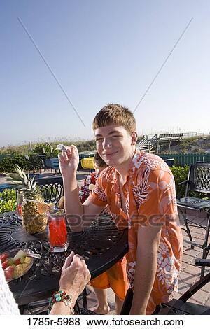 Portrait of a teenage boy in a tropical shirt sitting at a table enjoying some drinks and fresh fruit View Large Photo Image Stock Photo - Portrait of a teenage boy in a tropical shirt sitting at a table enjoying some drinks and fresh fruit. Fotosearch