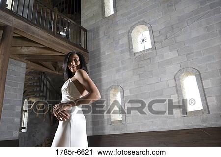 Stock Image - Portrait of a young bride in a white gown standing inside a medieval castle. Fotosearch