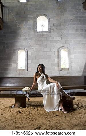 Stock Photography - Portrait of a young bride in a white gown sitting on a bench inside a medieval castle. Fotosearch
