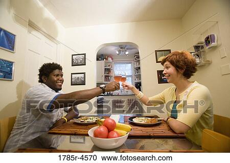 Portrait of a young inter-racial couple sitting at dining table toasting with glasses of wine View Large Photo Image Stock Image - Portrait of a young inter-racial couple sitting at dining table toasting with glasses of wine. Fotosearch