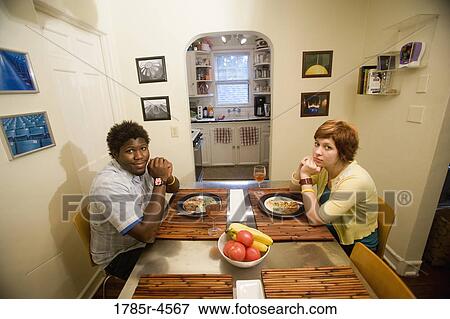 Stock Photo - Portrait of a young inter-racial couple sitting at dining table. Fotosearch