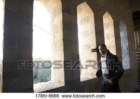Portrait of a young man in a black tuxedo leaning against a large window inside a medieval castle View Large Photo Image Stock Photograph - Portrait of a young man in a black tuxedo leaning against a large window inside a medieval castle. Fotosearch