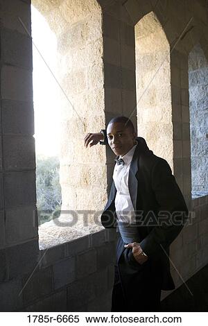 Stock Photography - Portrait of a young man in a black tuxedo leaning against a large window inside a medieval castle. Fotosearch