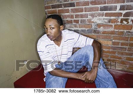 Portrait of a young man in hip-hop fashion sitting against brick wall View Large Photo Image Stock Image - Portrait of a young man in hip-hop fashion sitting against brick wall. Fotosearch