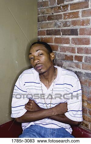 Portrait of a young man in hip-hop fashion sitting against brick wall View Large Photo Image Stock Image - Portrait of a young man in hip-hop fashion sitting against brick wall. Fotosearch