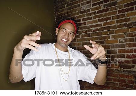 Stock Image - Portrait of a young man in hip-hop fashion standing showing gangsta hand gestures. Fotosearch