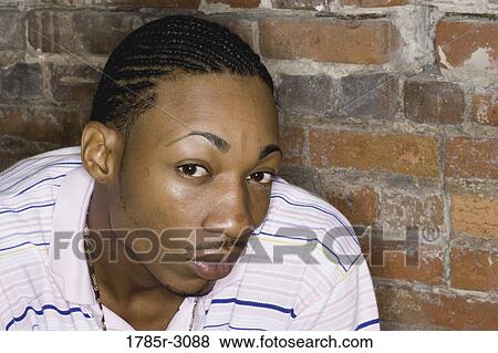 Portrait of a young man in hip-hop fashion sitting against brick wall View Large Photo Image Stock Photo - Portrait of a young man in hip-hop fashion sitting against brick wall. Fotosearch