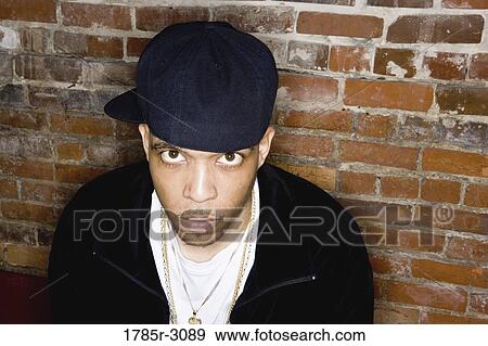 Portrait of a young man in hip-hop fashion sitting against brick wall View Large Photo Image Stock Photo - Portrait of a young man in hip-hop fashion sitting against brick wall. Fotosearch
