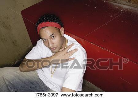 Stock Photo - Portrait of a young man in hip-hop fashion sitting on the floor. Fotosearch