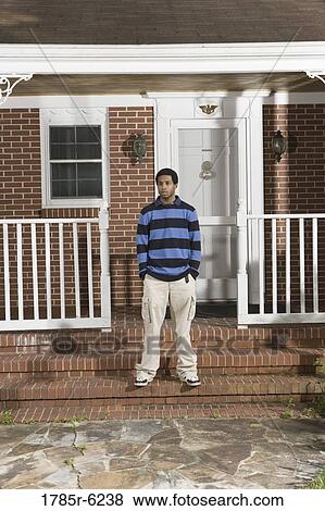 Stock Photo - Portrait of a young man standing on front porch of house. Fotosearch
