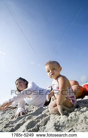 Stock Photo - Portrait of baby girl sitting with mother on sand at beach. Fotosearch