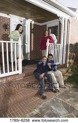 Stock Photo - Portrait of brothers sitting on front steps of house with family behind. Fotosearch
