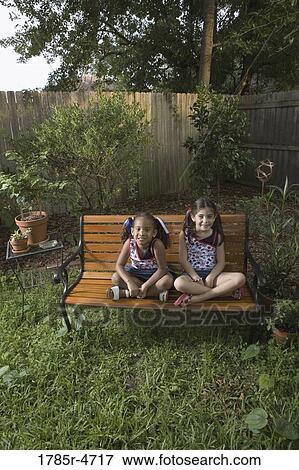 Portrait of cheerful girls (6-7) sitting on a bench in a backyard View Large Photo Image Stock Photo - Portrait of cheerful girls (6-7) sitting on a bench in a backyard. Fotosearch