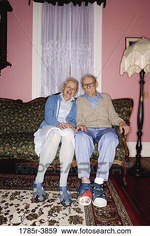 Portrait of cheerful senior couple sitting and separated on sofa in living room View Large Photo Image Stock Photo - Portrait of cheerful senior couple sitting and separated on sofa in living room. Fotosearch