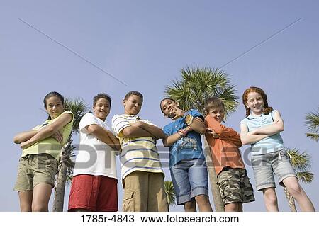 Stock Image - Portrait of children with folded arms standing abreast at a playground. Fotosearch