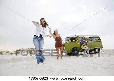Stock Image - Portrait of hippies dancing and playing guitar on the beach. Fotosearch