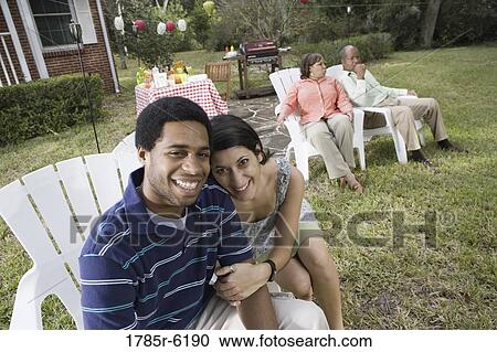 Stock Image - Portrait of interracial couple sitting together with parents background. Fotosearch