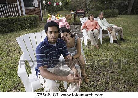 Stock Photo - Portrait of interracial couple sitting together with parents background. Fotosearch