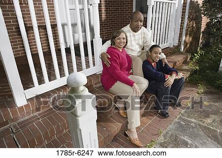 Stock Photo - Portrait of mature couple and their son sitting on front steps of house. Fotosearch