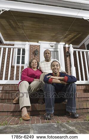 Stock Photo - Portrait of mature couple and their son sitting on front steps of house. Fotosearch