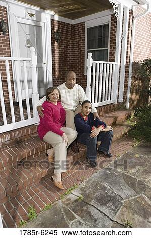 Stock Photography - Portrait of mature couple and their son sitting on front porch of house. Fotosearch