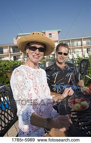 Portrait of mature couple in tropical outfits sitting at a table with hotel in the background View Large Photo Image Stock Photo - Portrait of mature couple in tropical outfits sitting at a table with hotel in the background. Fotosearch