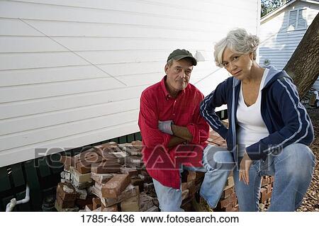 Stock Photograph - Portrait of mature couple next to stack of bricks outside house. Fotosearch