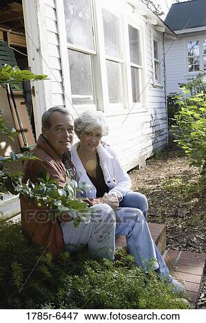 Stock Photo - Portrait of mature couple sitting on doorstep of dilapidated tool shed. Fotosearch