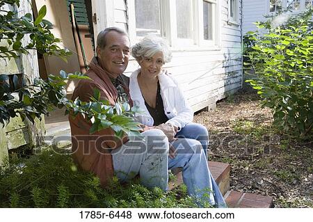 Stock Photo - Portrait of mature couple sitting on doorstep of dilapidated tool shed. Fotosearch