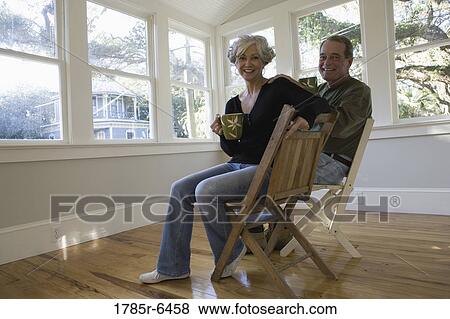 Stock Photo - Portrait of mature couple sitting inside renovated house. Fotosearch