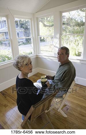 Stock Photograph - Portrait of mature couple sitting inside renovated house. Fotosearch