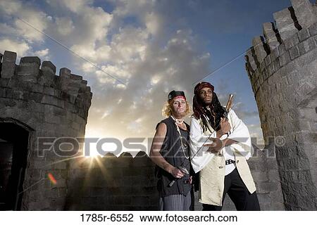 Stock Image - Portrait of pirates armed with a pistol and a sword with castle turrets and parapets in the background. Fotosearch