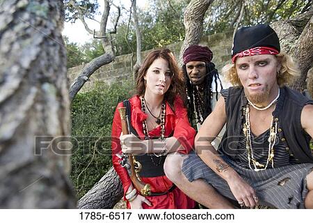 Stock Photo - Portrait of pirates sitting under trees with woman pirate holding a gun. Fotosearch