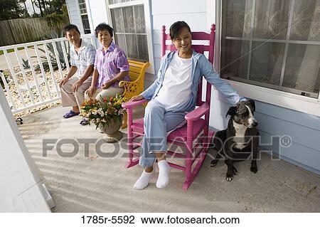 Stock Image - Portrait of pregnant woman sitting on rocking chair with her parents seated in background. Fotosearch