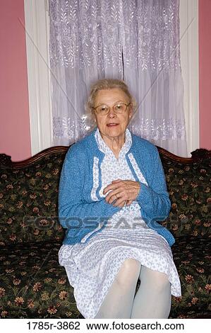 Stock Image - Portrait of senior woman sitting on sofa in living room. Fotosearch