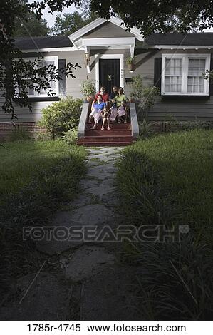 Stock Photography - Portrait of two families sitting on the front steps of a house waving US flags. Fotosearch