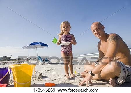 Stock Photo - Portrait of young father and daughter playing with shovels and buckets on the beach. Fotosearch