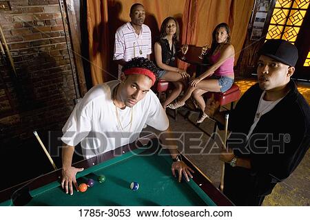 Stock Image - Portrait of young men in hip-hop fashion leaning against pool table. Fotosearch