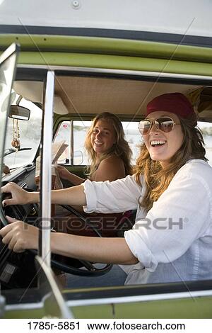 Stock Image - Portrait of young women in hippie fashion driving van at beach. Fotosearch