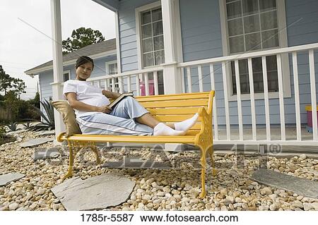 Pregnant woman laying on a bench reading a book in front of house View Large Photo Image Stock Photo - Pregnant woman laying on a bench reading a book in front of house. Fotosearch