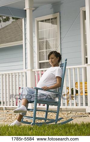 Picture - Pregnant woman sitting on a rocking chair in front of house. Fotosearch
