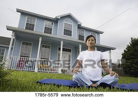 Stock Photo - Pregnant woman sitting on exercise mat in front of house. Fotosearch