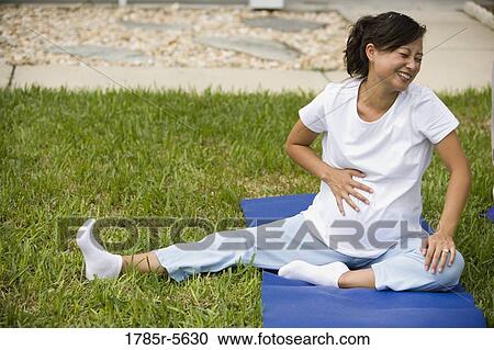 Stock Image - Pregnant woman sitting on yoga mat laughing. Fotosearch