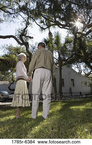 Rear view of mature couple holding hands under oak trees View Large Photo Image Picture - Rear view of mature couple holding hands under oak trees. Fotosearch