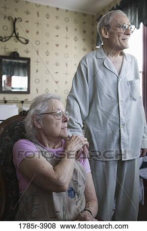 Seated senior woman affectionately patting senior man's hand that is resting on her shoulder View Large Photo Image Stock Photo - Seated senior woman affectionately patting senior man's hand that is resting on her shoulder. Fotosearch