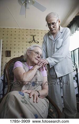 Stock Photo - Seated senior woman affectionately patting senior man's hand that is resting on her shoulder. Fotosearch